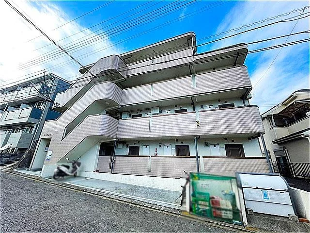 3階建てのアパートメントの外観。バルコニーと階段付きで、周囲に電線が張っている。