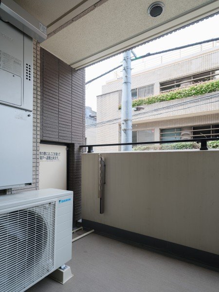 アパートのベランダの風景。空調ユニットと壁、隣の建物と電柱が見える。
