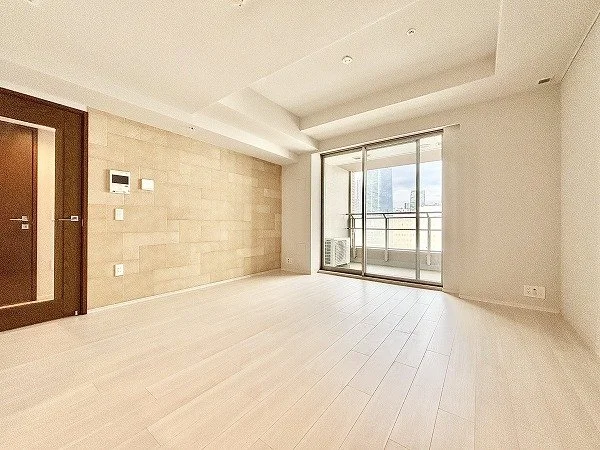 白い壁と木製の床の空室リビングルーム、窓側にバルコニーへのガラス扉と外の景色が見える