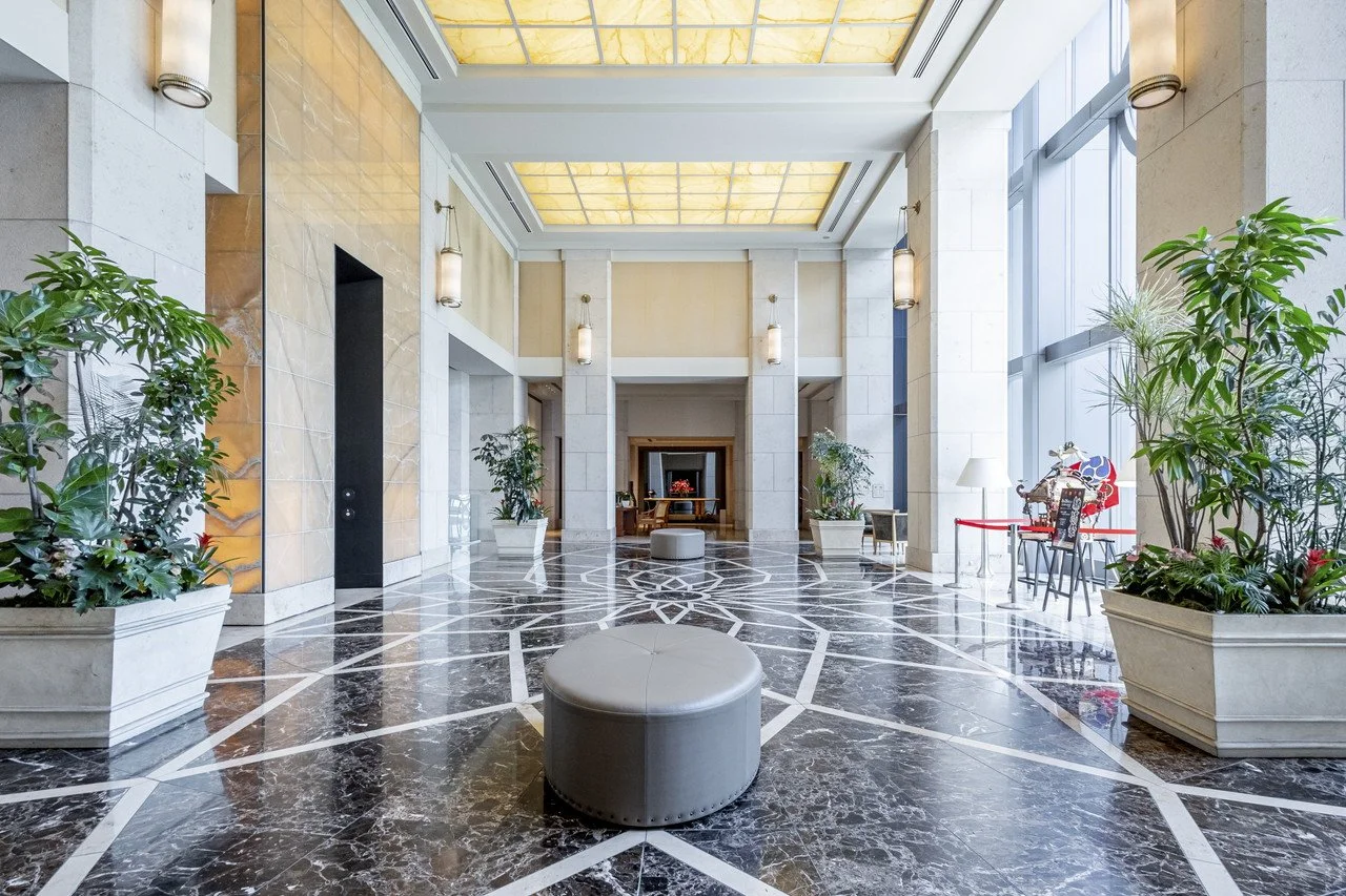 高級ホテルのロビー入口、石とガラスの壁、花の置物、大きな窓、植物、座るためのクッションと椅子、照明器具。