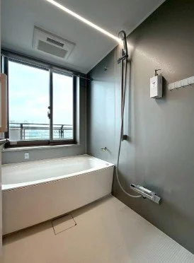 浴室のバスタブとシャワー、窓と壁に設置された換気扇とシャワーコントローラーが映っています。