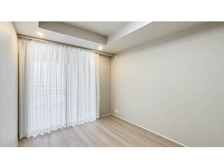 白い壁と木製フローリングの空き部屋、カーテン越しに自然光が差し込んでいる