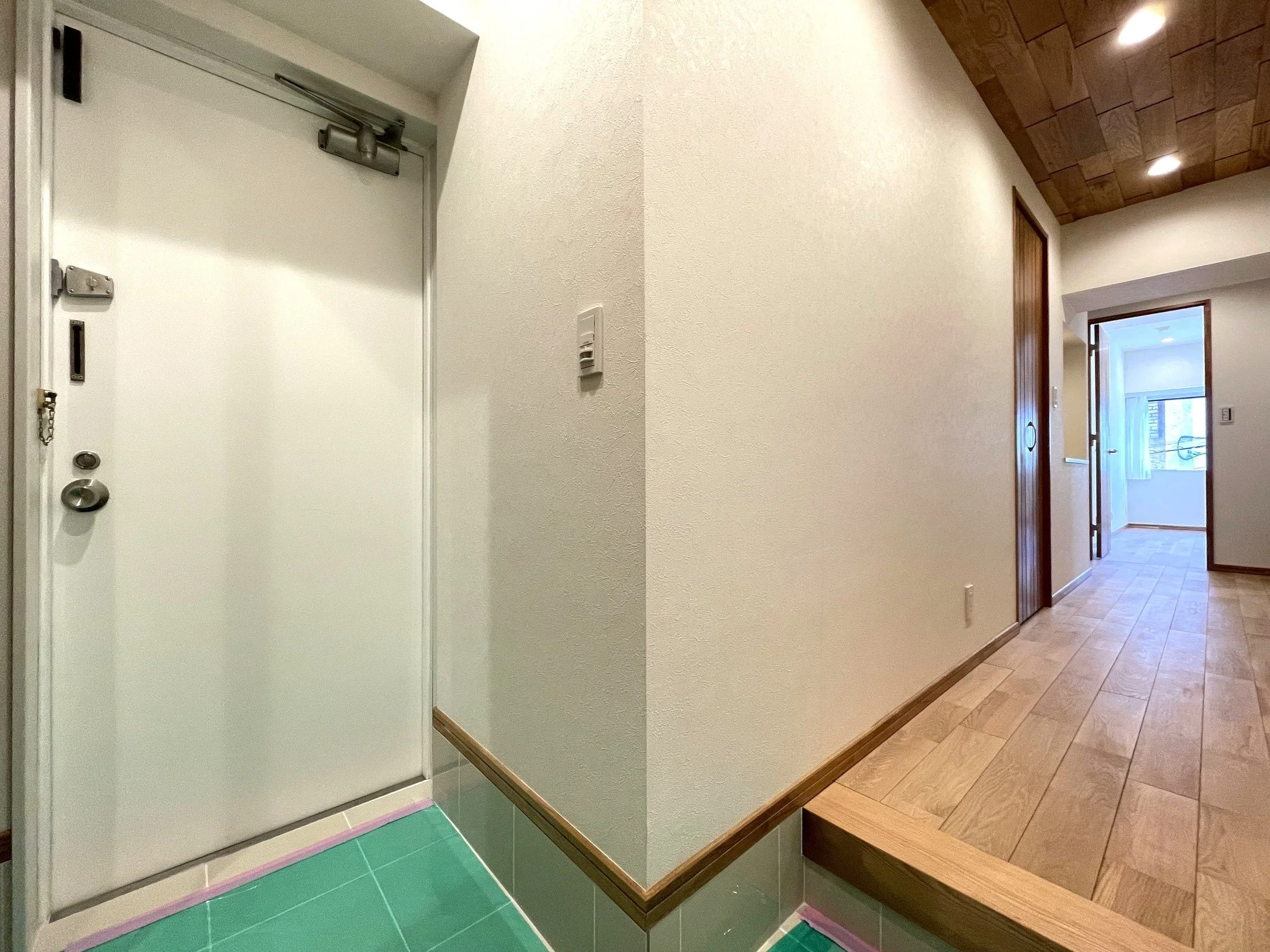 玄関の入り口と廊下、木の床と壁、天井の照明が見える内装の写真