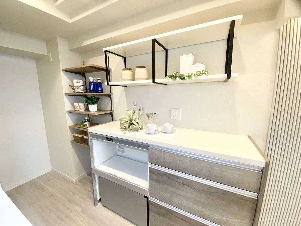 白いキッチンのカウンターと棚に装飾品や食器が置かれている写真。