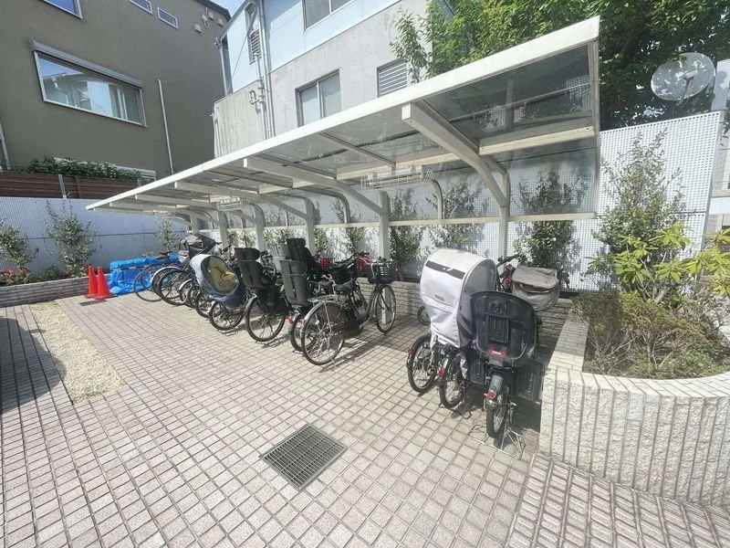 屋根のある自転車駐輪場に複数の自転車が停められている。背景に建物と木々が見える。