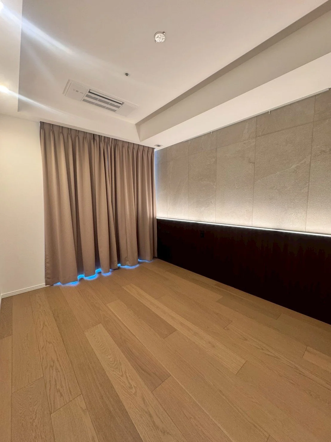 木製の床とベージュのカーテン、壁紙と間接照明が施されたシンプルでモダンな室内空間