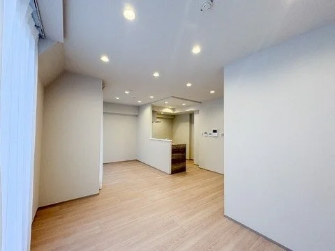 空の白い壁と木製フローリングの部屋。天井には複数の埋め込み照明がある。