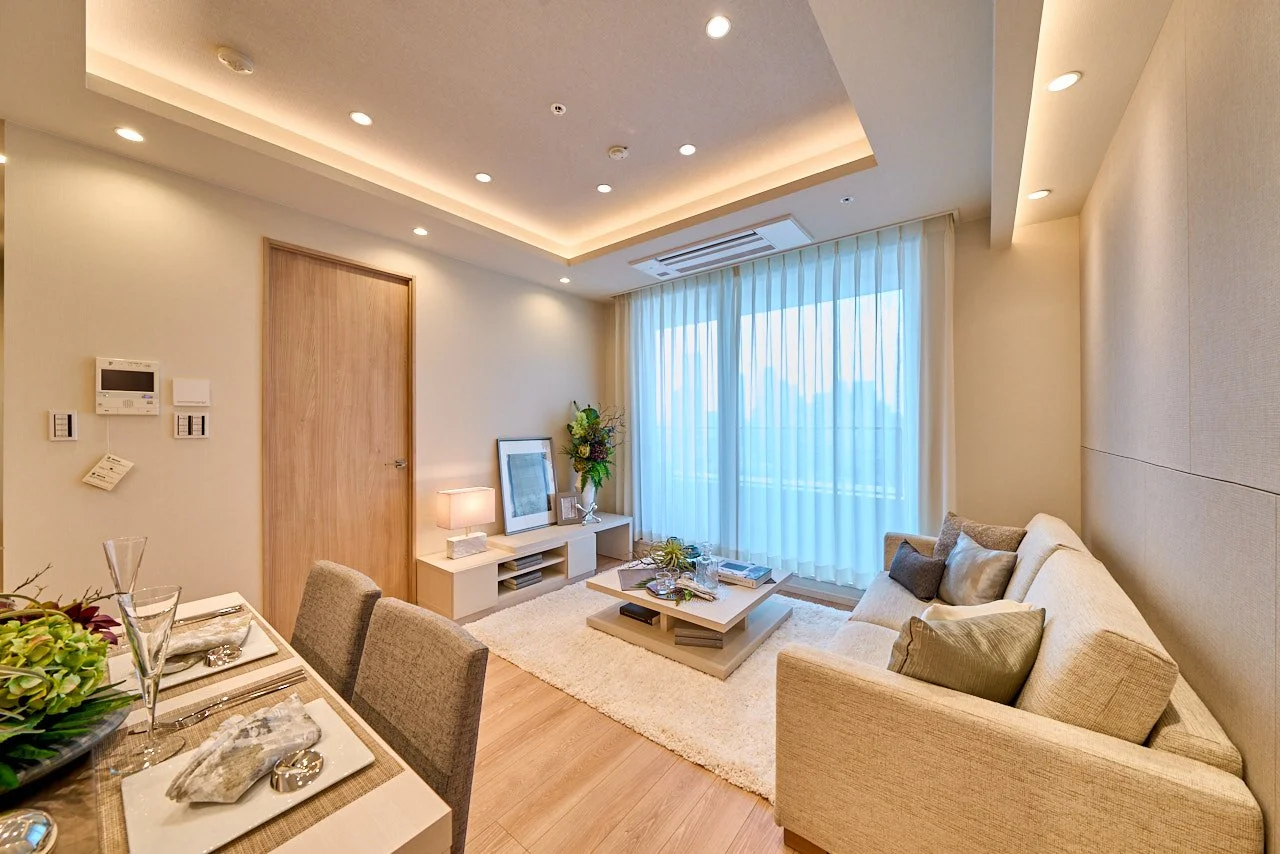 シンプルでモダンなリビングルームの interior with beigeのソファとダイニングテーブル、窓辺にカーテン、テーブルにお皿とグラス、壁に装飾や照明