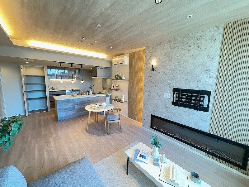 現代的なリビングルームとキッチンの画像。木製の床と天井で、オープンプランの空間。ソファ、コーヒーテーブル、壁にテレビとガスコンロ。