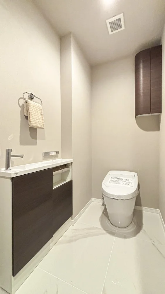 トイレのあるシンプルで清潔な洗面所、タオルと小さな洗面台が壁に設置されている所.