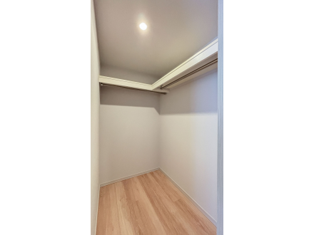 空っぽのクローゼットの中の写真です。木製の床と白い壁、天井に照明があります。