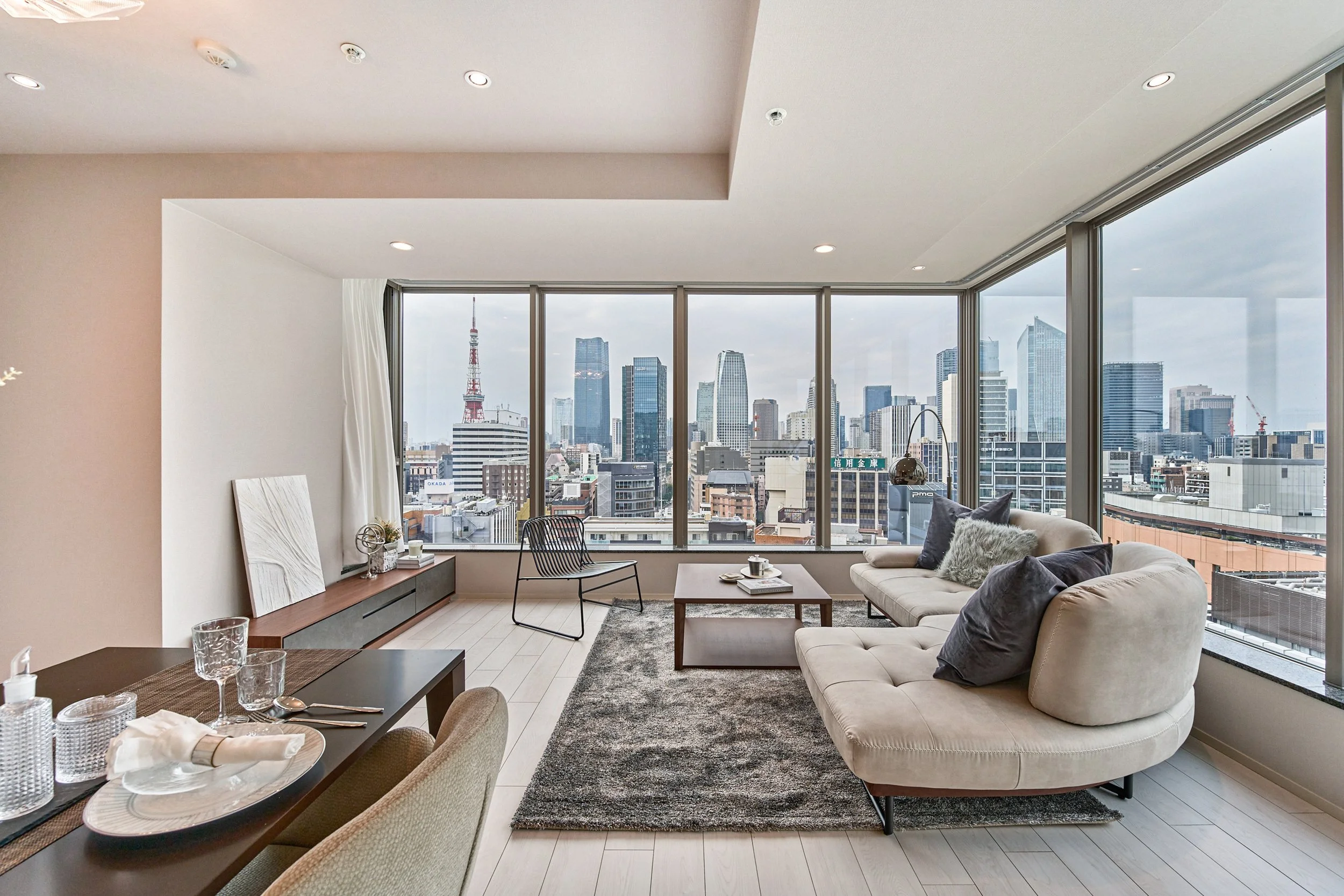 広々としたリビングルームから東京の高層ビルの眺め。Large living room with sofa, coffee table, dining table, and large windows showing Tokyo skyline.