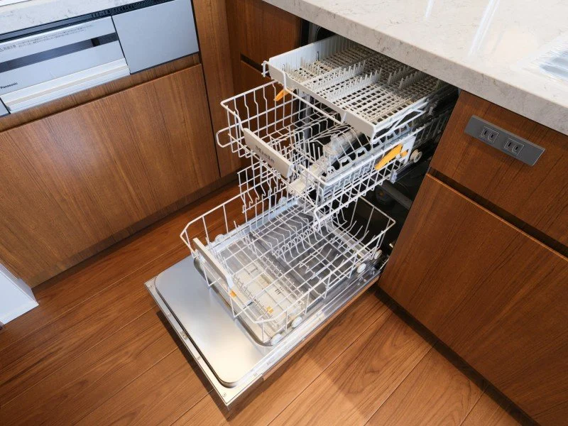食器洗い機のドアが開いているキッチンの様子。中に空のラックと、一部の食器や調理器具が見える。