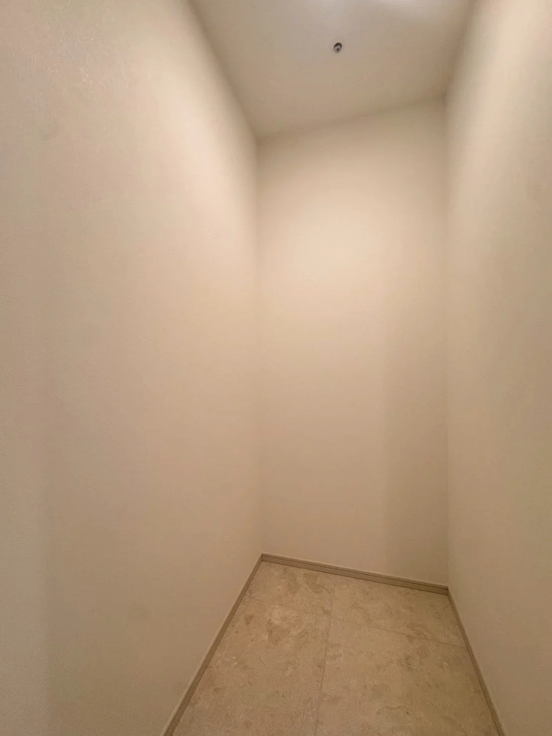 白い壁の小さな角部屋、天井に照明の取り付け穴、床は大理石のタイル