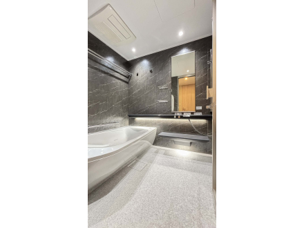 モダンなバスルームの写真。黒いタイルの壁と白い浴槽、鏡と洗面台があります。