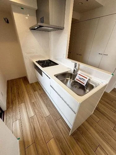 白いキッチンのカウンターとシンク、コンロ、木目調の床と白い収納棚