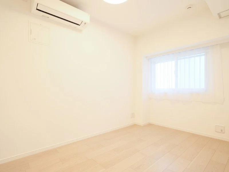 白い壁と木製の床、窓とエアコンがある空き部屋。