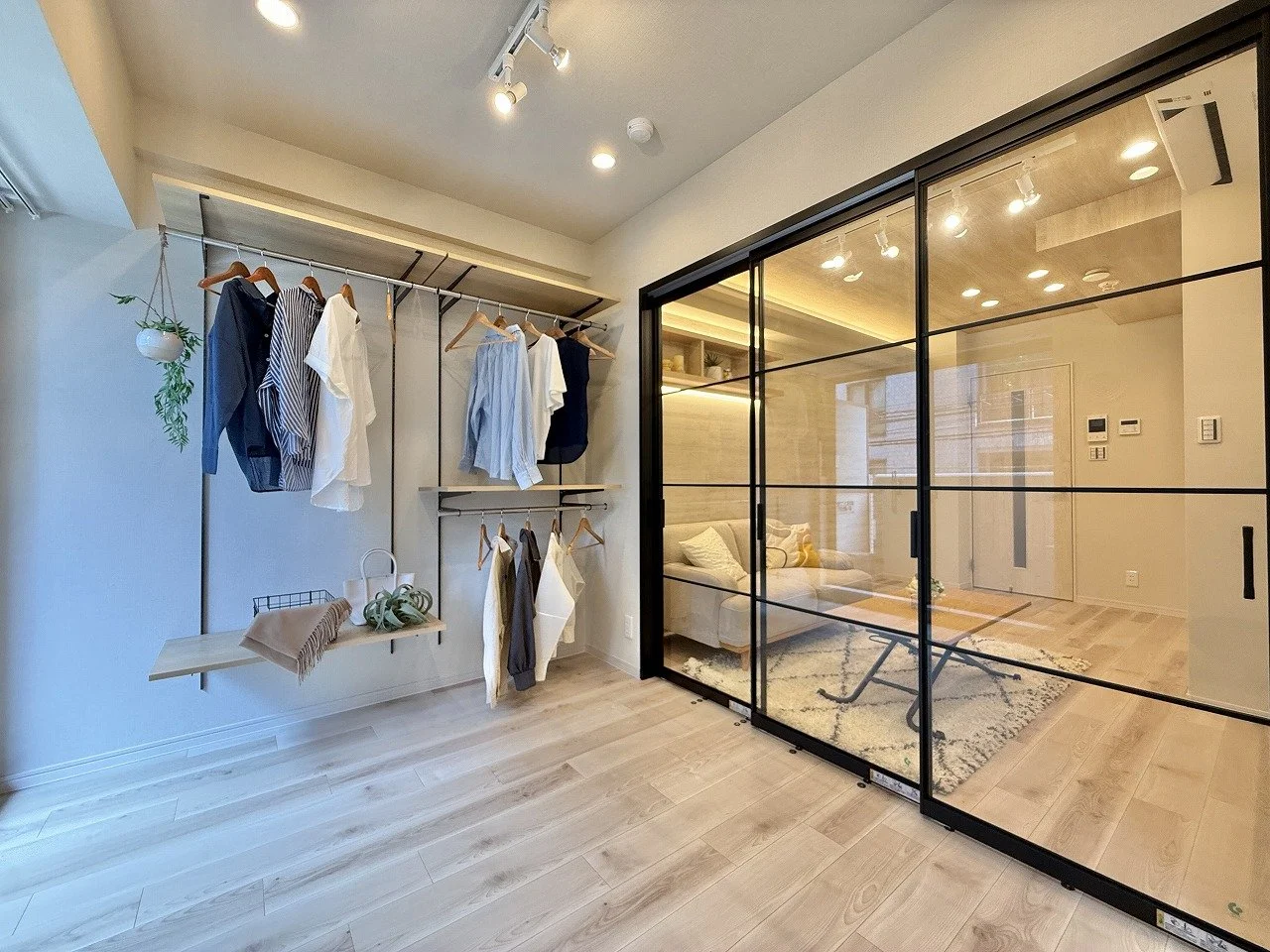 服が掛けられたクローゼットとリビングルームが見える仕切りガラスのある部屋の内装