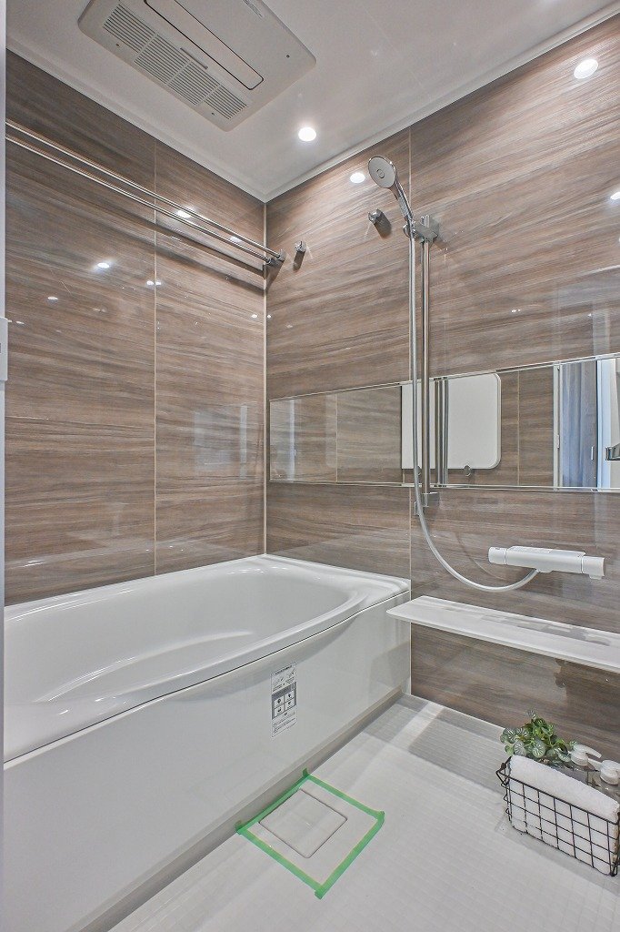 木目調の壁面に白いバスタブとシャワー、鏡と棚、バスルームの天井に換気扇がある浴室の画像。