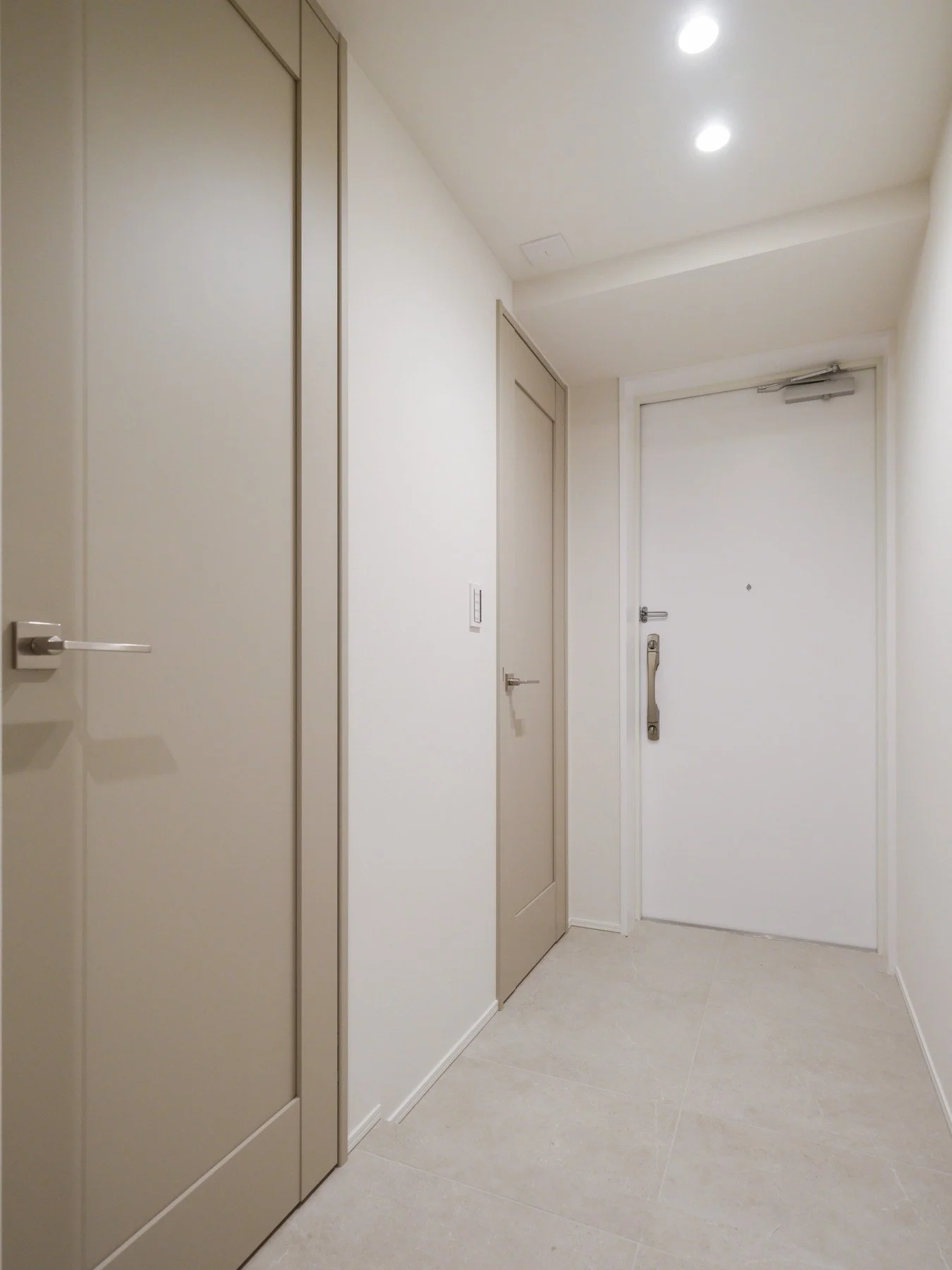 シンプルな玄関ドアと収納扉がある室内の画像。照明が点灯している。