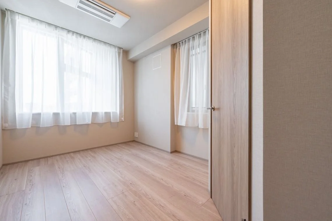 明るい日差しが差し込む空のカーテンのついた空の部屋に木の床と木の扉がある部屋の内部