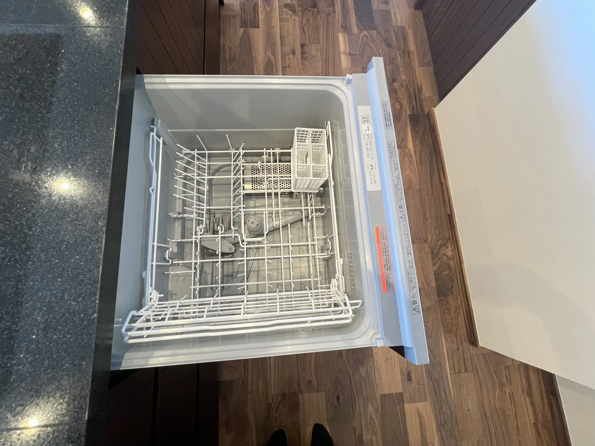 空の食器洗い機。木製の床と白い壁の前に設置されている。