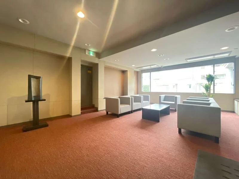 明るい窓辺のラウンジエリア、白い椅子とコーヒーテーブルが配置されている、観葉植物と雲のような天井の照明あり