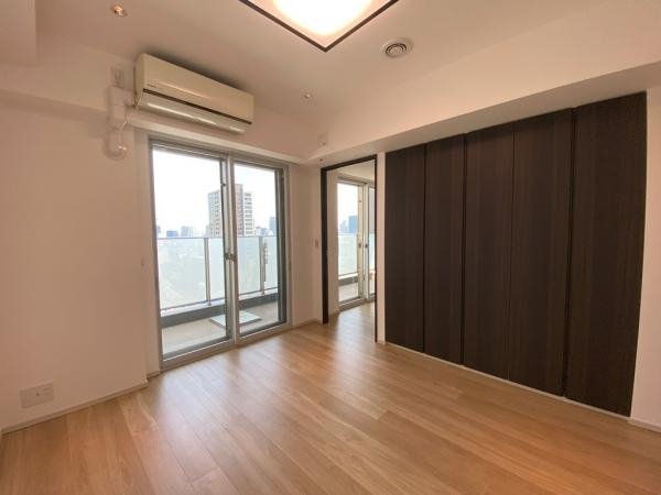 空の部屋に大きな窓とバルコニー、木製の床と壁収納、エアコンが設置されている