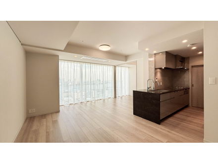 リビングルームとキッチンの広い空間、窓から自然光が入るシンプルな内装。