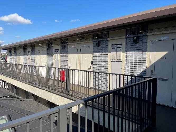 二階建てのアパートの外観。廊下には複数のドアとシャッターがあり、火災用の消火栓も見える。