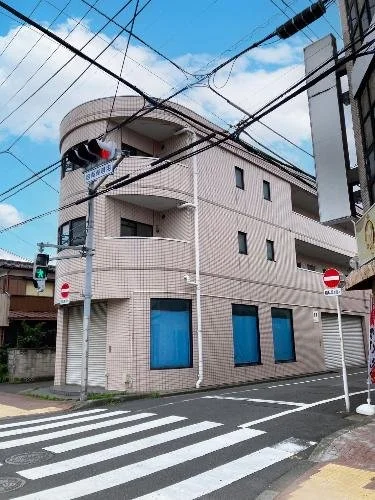 角にある白いレンガの3階建て建物。青い窓とバルコニー、交差点の信号と標識が見える。