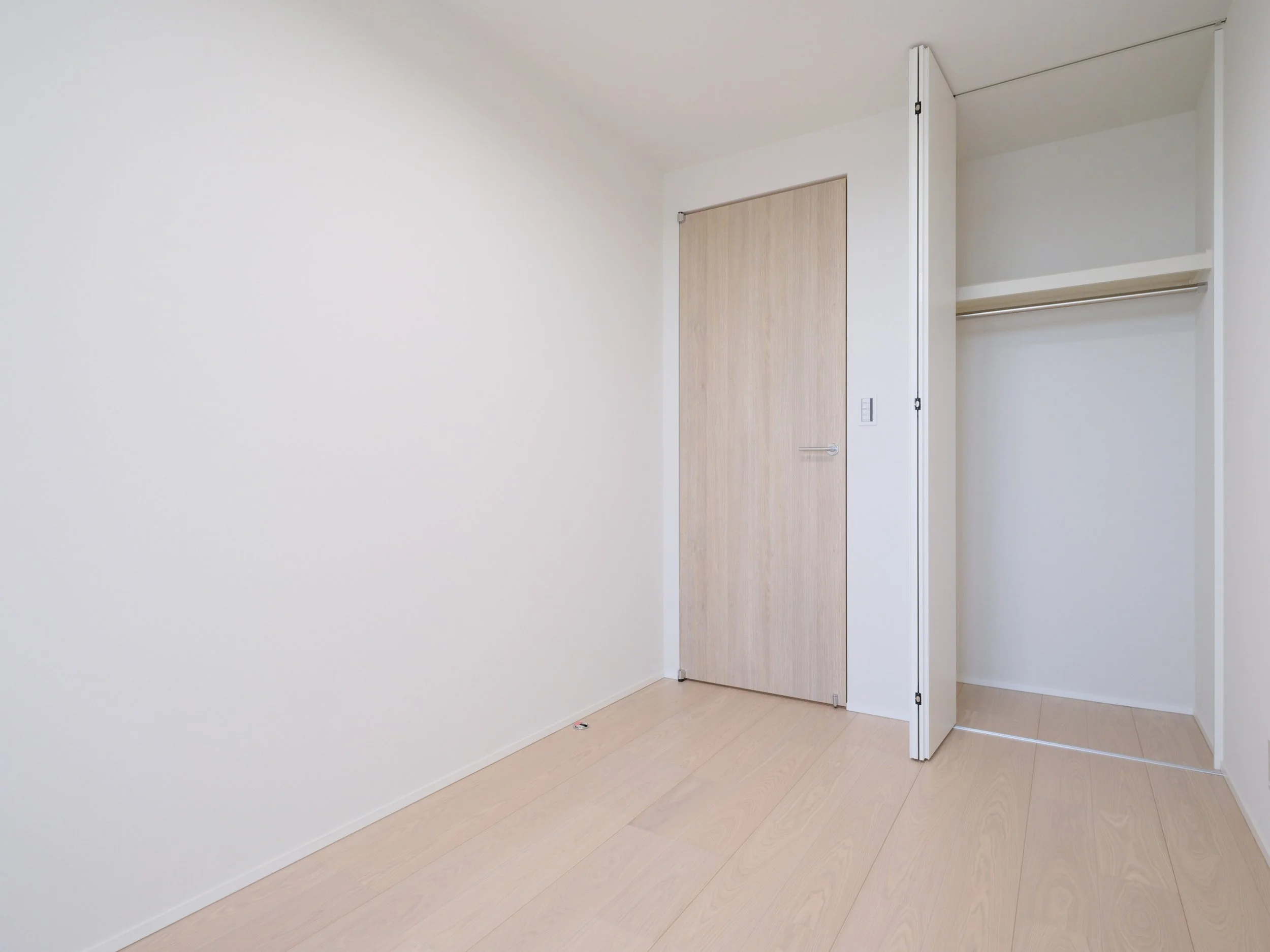 白い壁と木製の床、木製のドアと開いたクローゼットのある空室の部屋