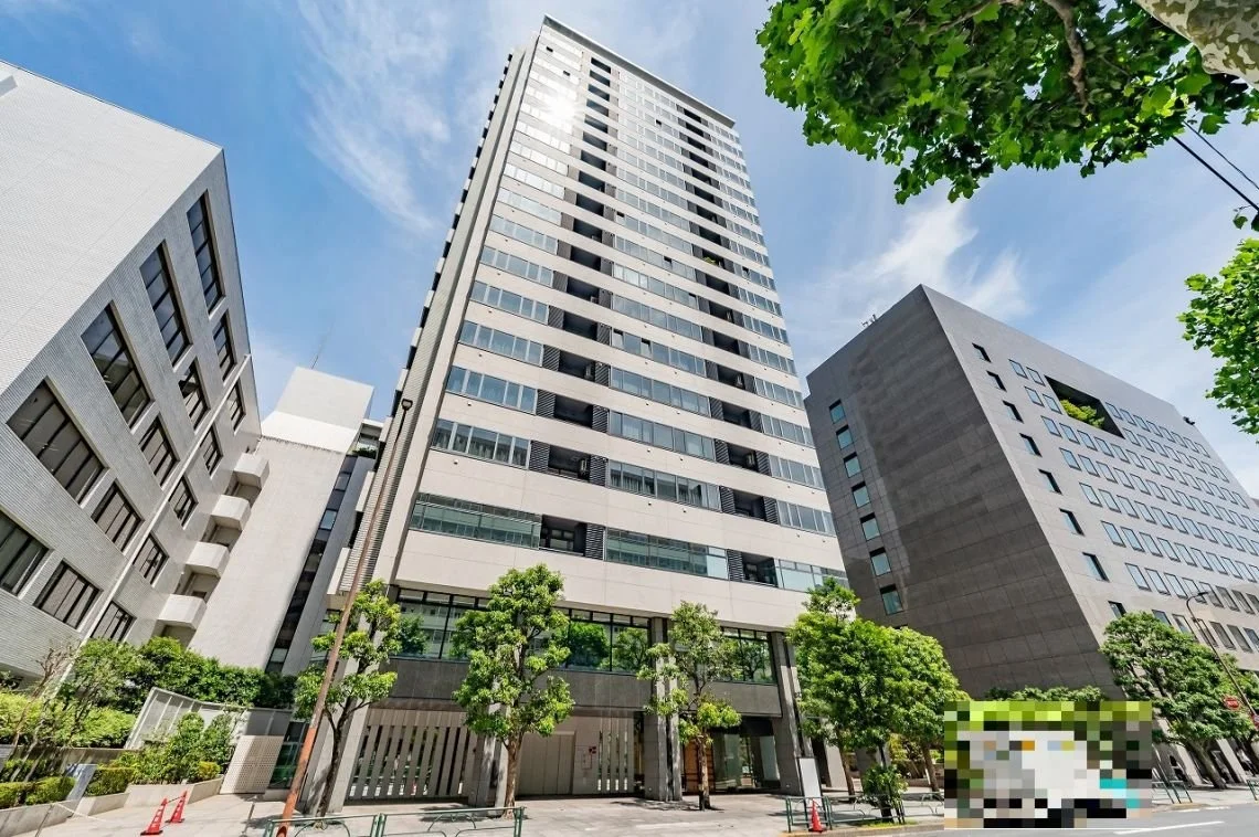 高層ビルが並ぶ都市の風景で、青空と周囲の緑の木々が写っている