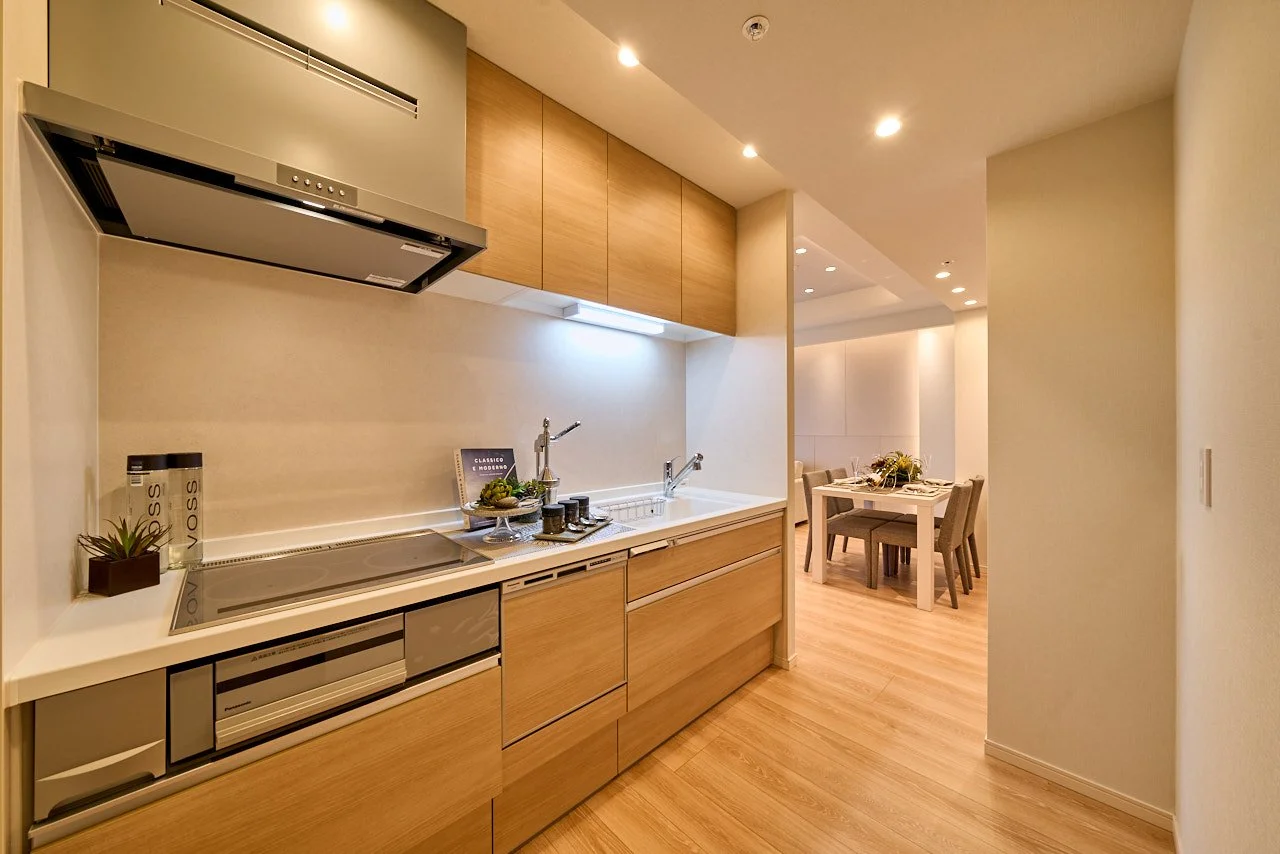 モダンなキッチンとダイニングルーム。木製のキャビネットとダイニングテーブル、照明が映える温かみのある空間.