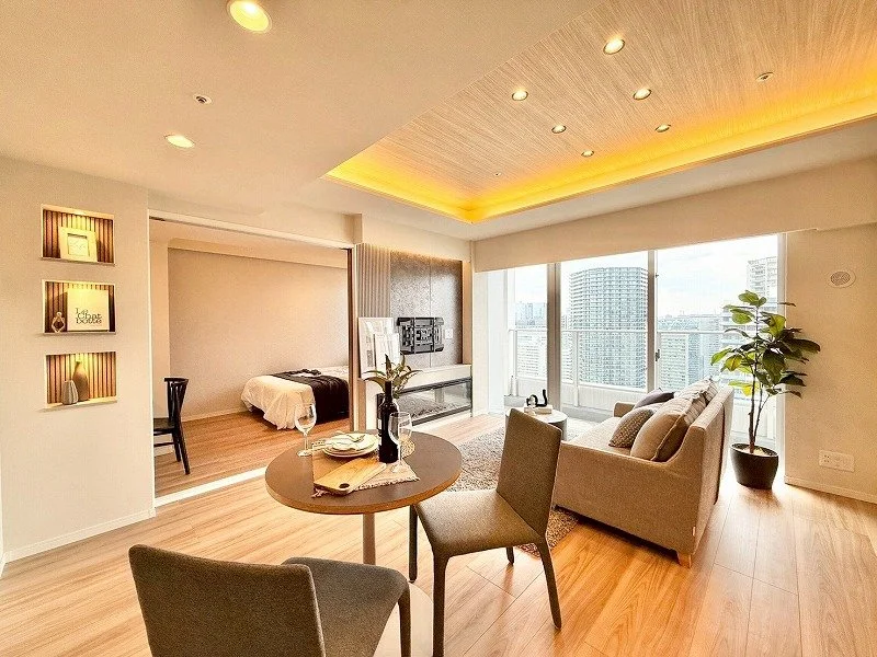 モダンなリビングルームとベッドルームが見える高層マンションの室内。ソファとダイニングテーブル、観葉植物が配置されている。