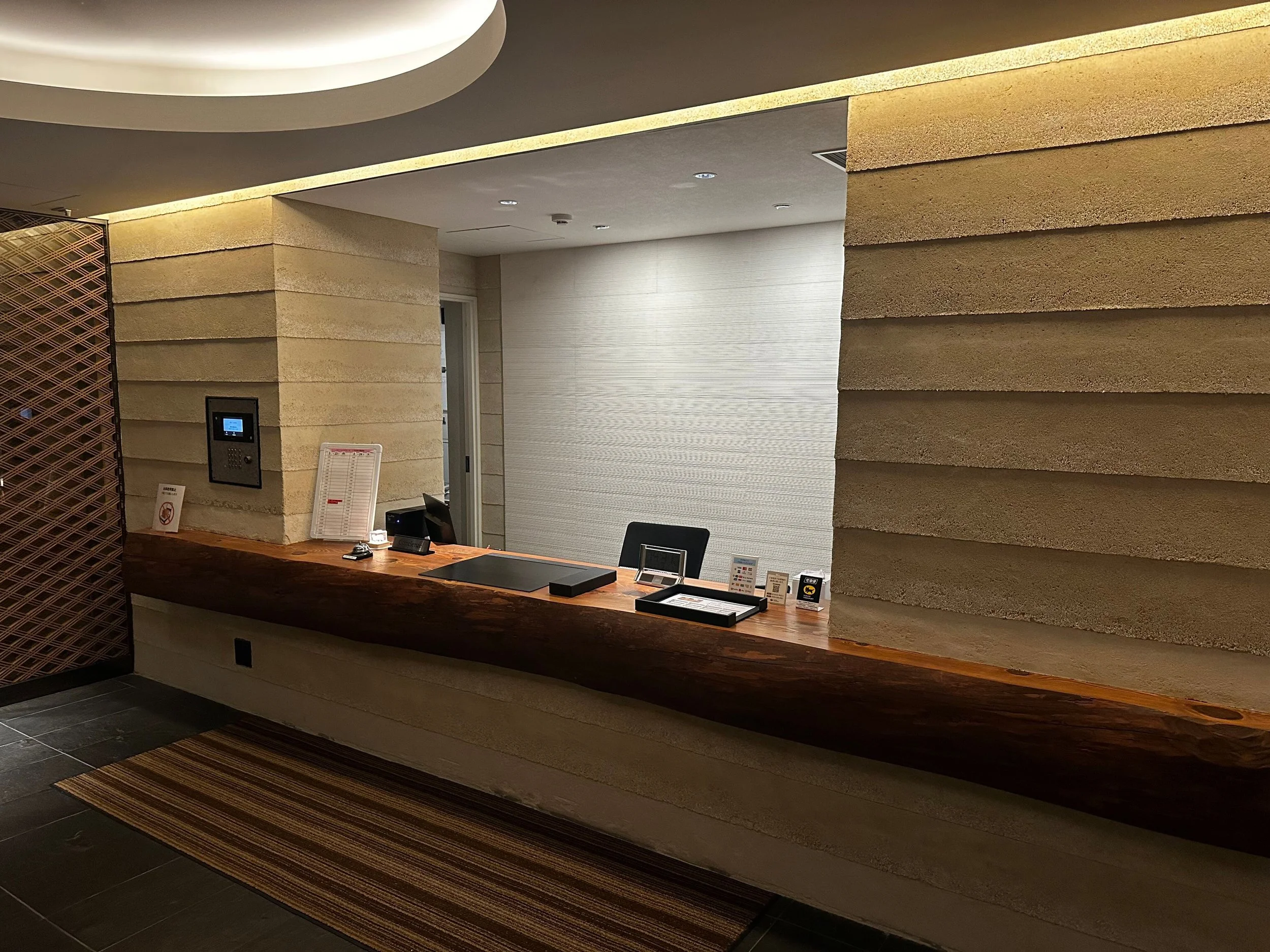 受付カウンターと壁の装飾がある室内の風景。カウンターの上には電話やメニューのような小物、壁にはスクリーンやサインが見える。