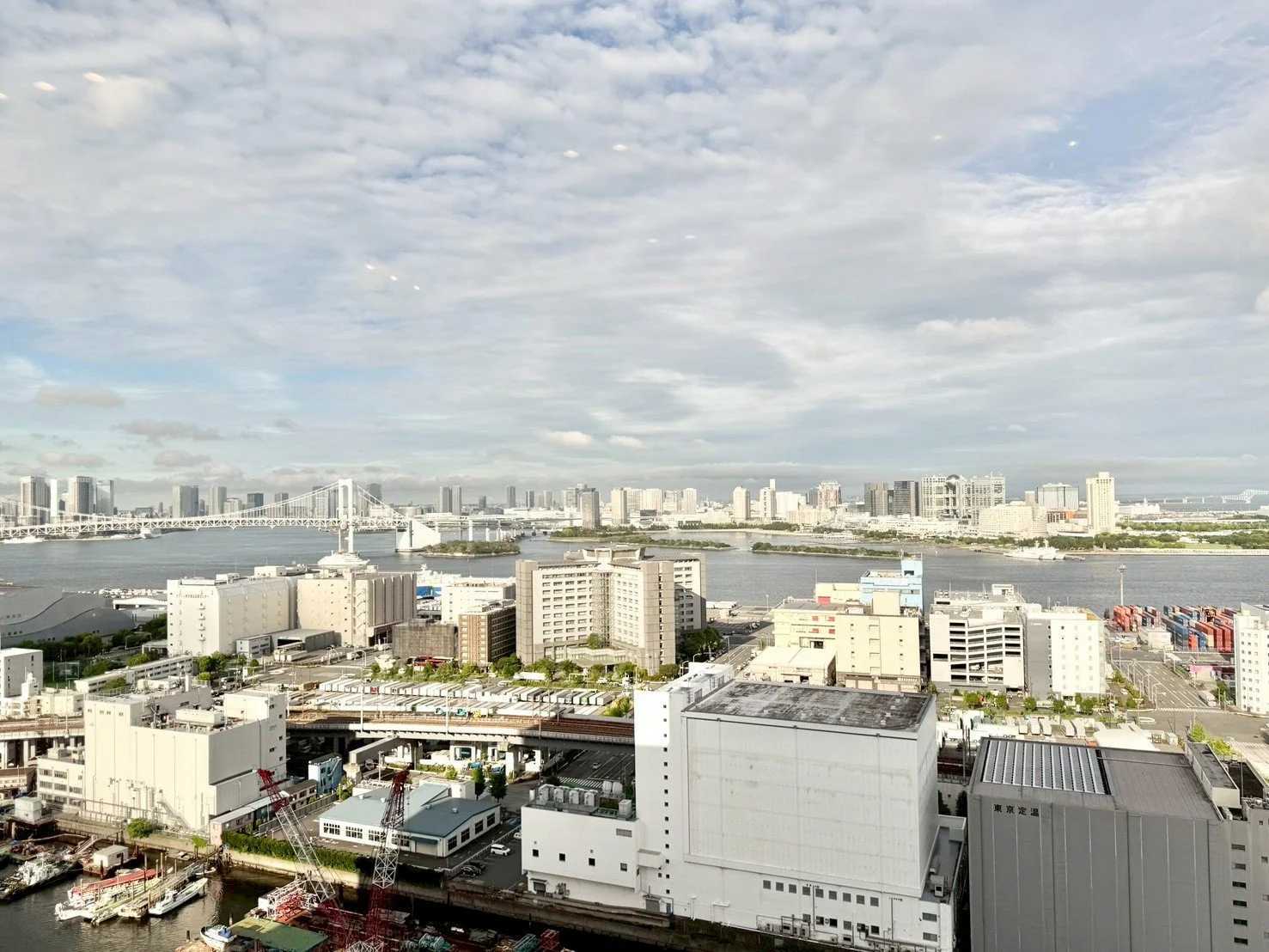 東京湾沿いの都市景観。橋と高層ビル群、空に浮かぶ雲を背景にした風景。