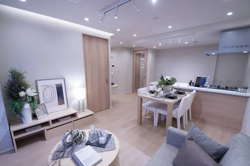 明るいリビングとダイニングキッチンのあるモダンな住宅内部。白い家具と木製の床、シンプルな装飾が特徴。
