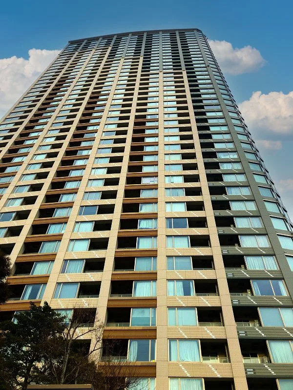 高層のマンションの外観、窓が並ぶ都市の建物、青空と雲の背景