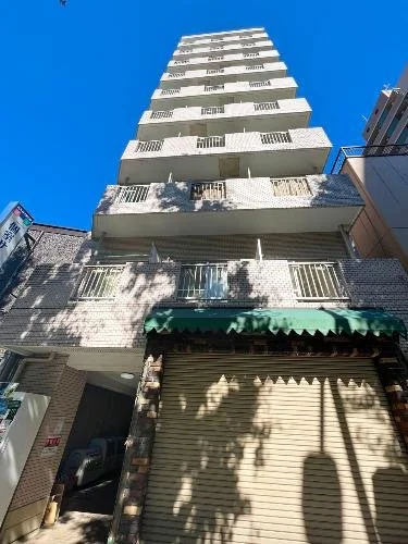 高層の白いコンクリートの建物と青い空、下にシャッター付きの小さな店を持つ建物