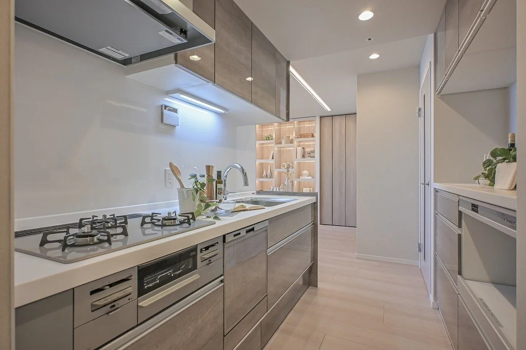 白いキッチンカウンターとシンク、ガスコンロ、木製の棚と収納棚があります。