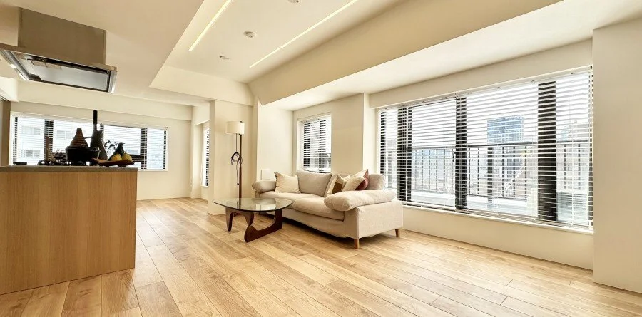 広々としたリビングルームで、大きな窓から自然光が差し込み、ソファと丸いコーヒーテーブルが配置されている。木製の床とシンプルなインテリアが特徴的です。