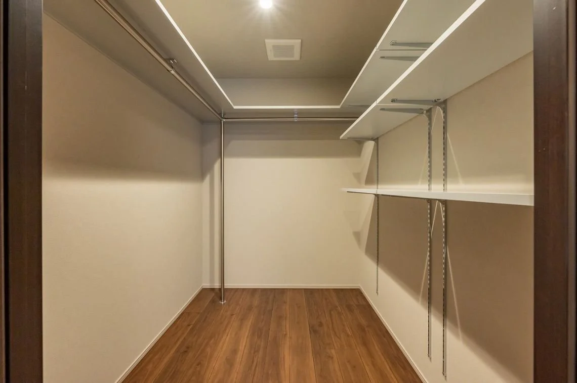 空のクローゼット収納棚とパイプ棚、木製の床と天井照明