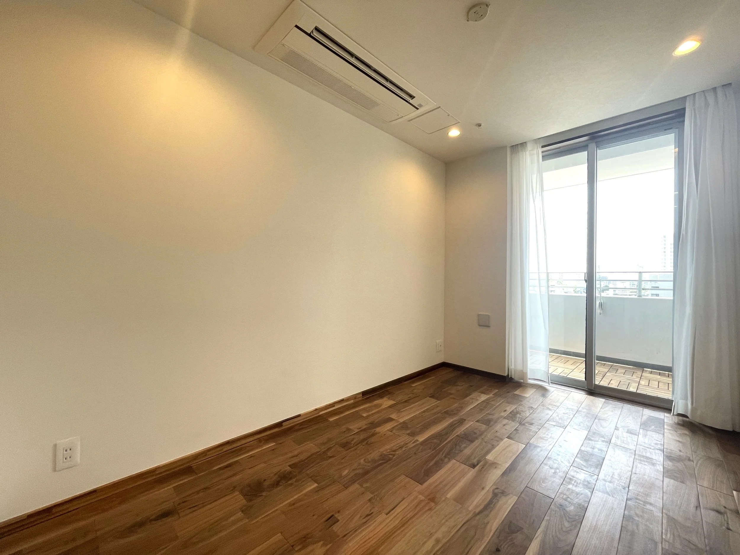 明るくて空っぽの部屋、木製の床と白い壁、窓の外にバルコニーが見える。