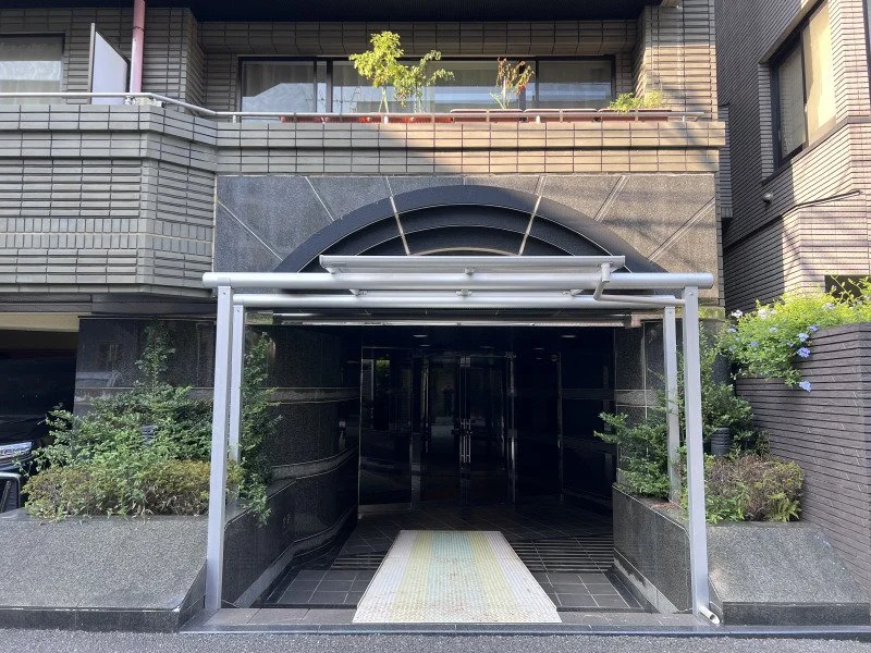 都市の建物の入り口、黒いガラスドアと花壇や植物が周囲にある