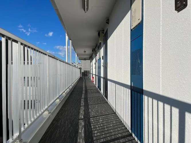 青空の下の高層建物の屋上の通路。金属製の白い手すりと壁に囲まれた長い廊下。