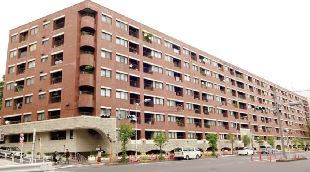 ブラウンの多階建てのマンションの建物。路上には車や人々が通っている。