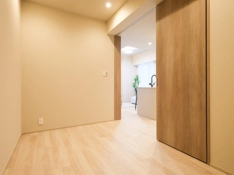 シンプルなリビングルーム、木製の扉とフローリング、窓から自然光が差し込み、観葉植物が見える。