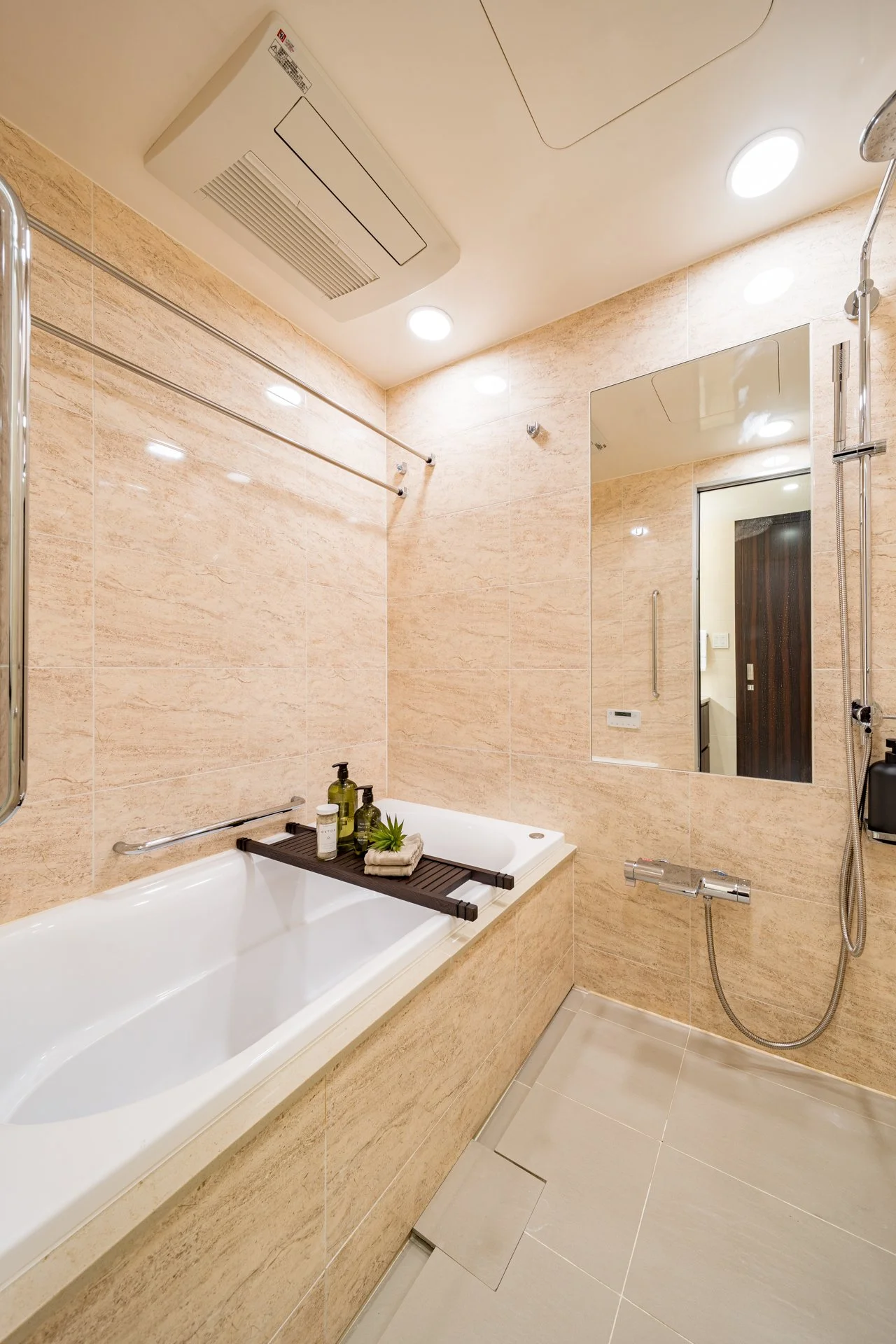 バスルームの浴槽にトレイとバス用品が置かれています。壁には鏡とシャワーがあります。