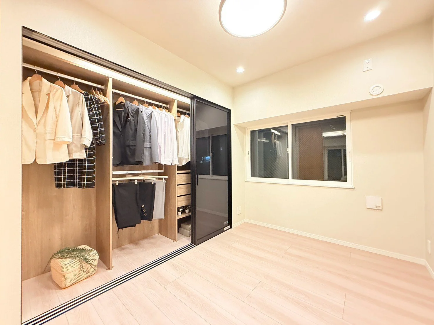 クローゼットにハンガーに掛けられた衣服とバッグ。部屋の壁には窓と照明があります。